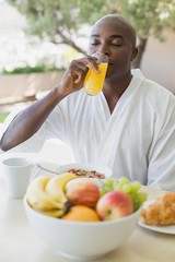 Obraz premium Handsome man in bathrobe having breakfast outside