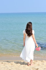 Fototapeta na wymiar 白いワンピースを着てピンクの花束を持って海に向かって立っている女性