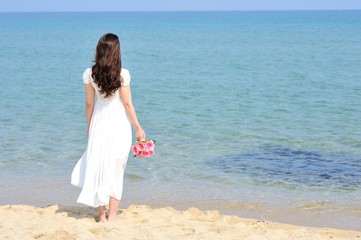 Fototapeta na wymiar 白いワンピースを着てピンクの花束を持って海に向かって立っている女性