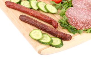 Sausage salami and vegetables on wooden platter.