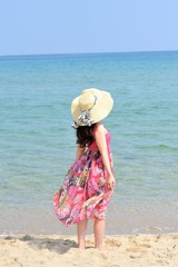 砂浜に麦わら帽子をかぶって立っている女性