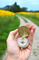 Compass in the hand against rural road - 67880564