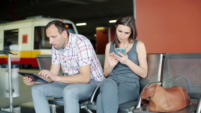Passengers with smartphone and tablet waiting at train station