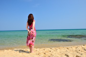 海を眺めるピンクのドレスを着た女性の後ろ姿