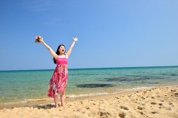 ピンクのワンピースを着て海で手を挙げているアジア人女性