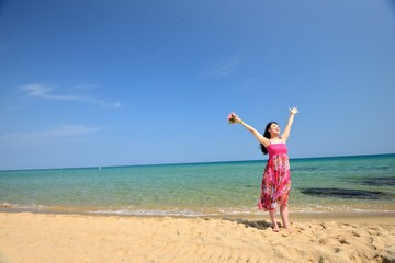ピンクのワンピースを着て海で手を挙げているアジア人女性