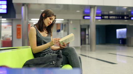 Young woman reading book, waiting at train station