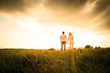 couple walking through the field and holding hands - obrazy, fototapety, plakaty