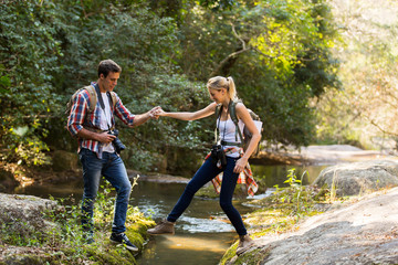 young man helping girlfriend crossing stream