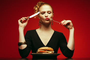Fashion & Gluttony Concept. Rred-haired model eating burger