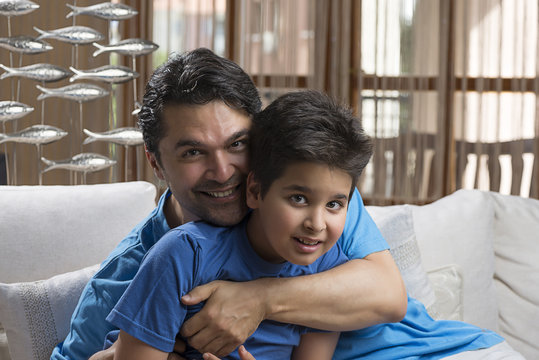 Adult man hugging his son while sitting at sofa