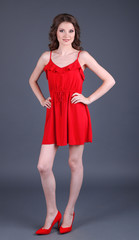 Beautiful young girl in red dress on grey background