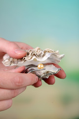 Hand with tweezers holding pearl and oyster on mature