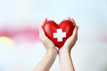 Red heart with cross sign in female hand, close-up,