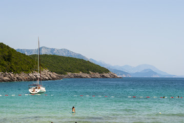 Fototapeta premium People in water; sailboat anchored by the coast