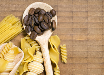 Kochlöffel mit Teigwaren und Kaffeebohnen auf einem Holzbrett