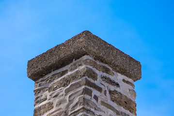 Brick and mortar chimney on blue sky.