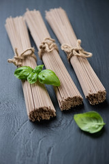Fototapeta na wymiar Dry buckwheat soba noodles with green basil leaves, studio shot