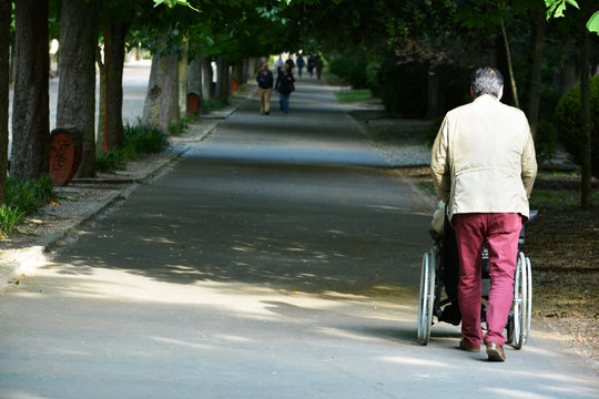 hombre empujando una silla de ruedas por un paseo urbano