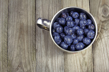 blueberries in metal cup on wooden background or texture