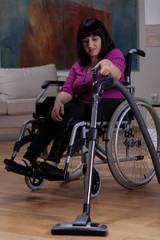 Fototapeta na wymiar Woman on wheelchair with vacuum cleaner