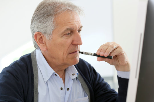 Senior Man Smoking With E-cigarette At Work