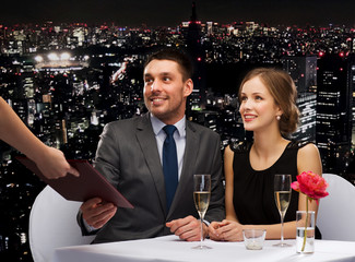 waiter giving menu to happy couple at restaurant