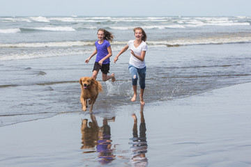 young girls running fast at the beach with a dog