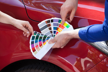 Mechanic Showing Color Samples To Customer Against Car