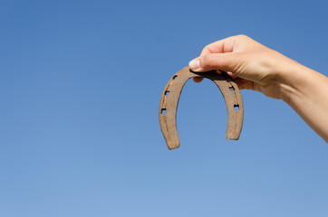 rusty iron horseshoe in hand on blue sky bckground
