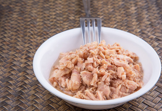 Pieces of canned tuna in a white bowl with a fork on wicker 