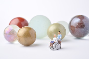 車椅子に乗っている高齢者と介助者のミニチュア人形
