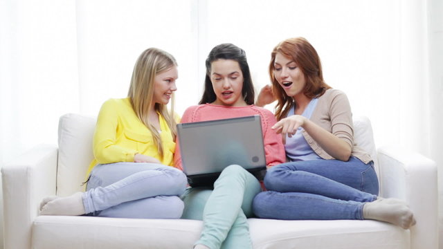 three smiling teenage girls with laptop at home