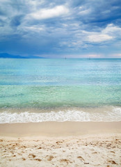Fototapeta na wymiar Sandy beach with clean blue waves and cloudy sky.