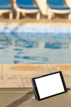 Blank digital tablet on a chair next to swimming pool