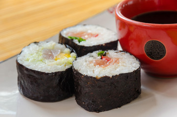 three sushi rolls with a small bowl of say sauce
