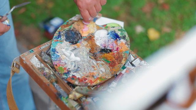 Artist squeezes the tube with oil paints on a palette