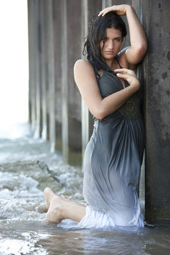 A young brunette female model posing in a wet dress at the beach on a sunny day.