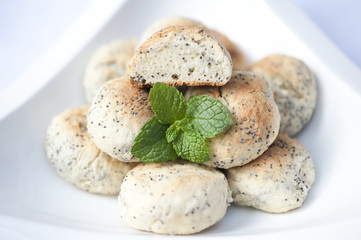 Handmade poppy seed cookies with a placed mint leaf on the side in a white bowl on a white background.