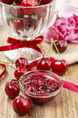 Bowl of cherry jam on wooden table and fresh cherries around