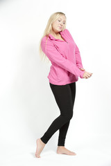 A happy young attractive female model wearing a pink sweatshirt with black pants on a white background.