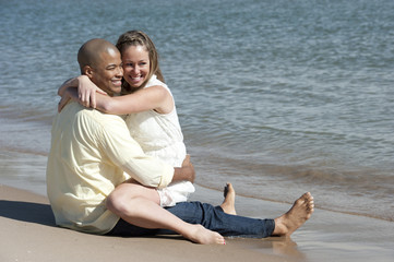 A romantic interracial couple sitting at the beach on a sunny day.