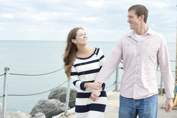 A young happy caucasian couple on a sunny day with the clouds in the background at the pier.