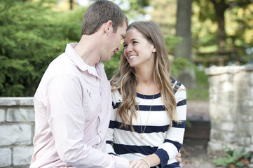 Happy young caucasian couple sitting at the park both hugging and smiling.