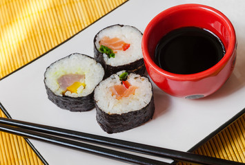 three sushi rolls with chopsticks and a bowl of soy sauce