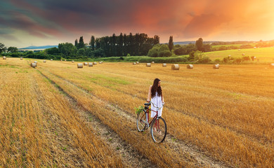 Beautiful woman pushes old red bike in a wheat field