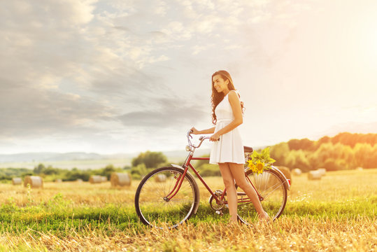 Beautiful woman with an old red bike in a wheat field
