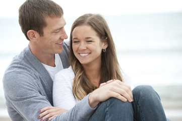 A young happy caucasian couple sitting on the sand at the beach on a sunny day.