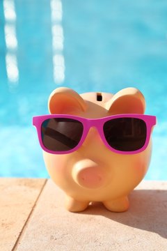 Summer piggy bank with sunglasses in front of a swimming pool