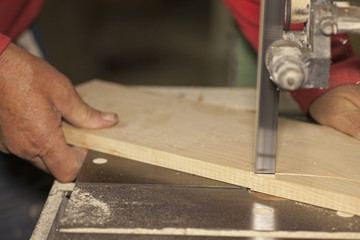 Carpenter sawing wood board on bandsaw